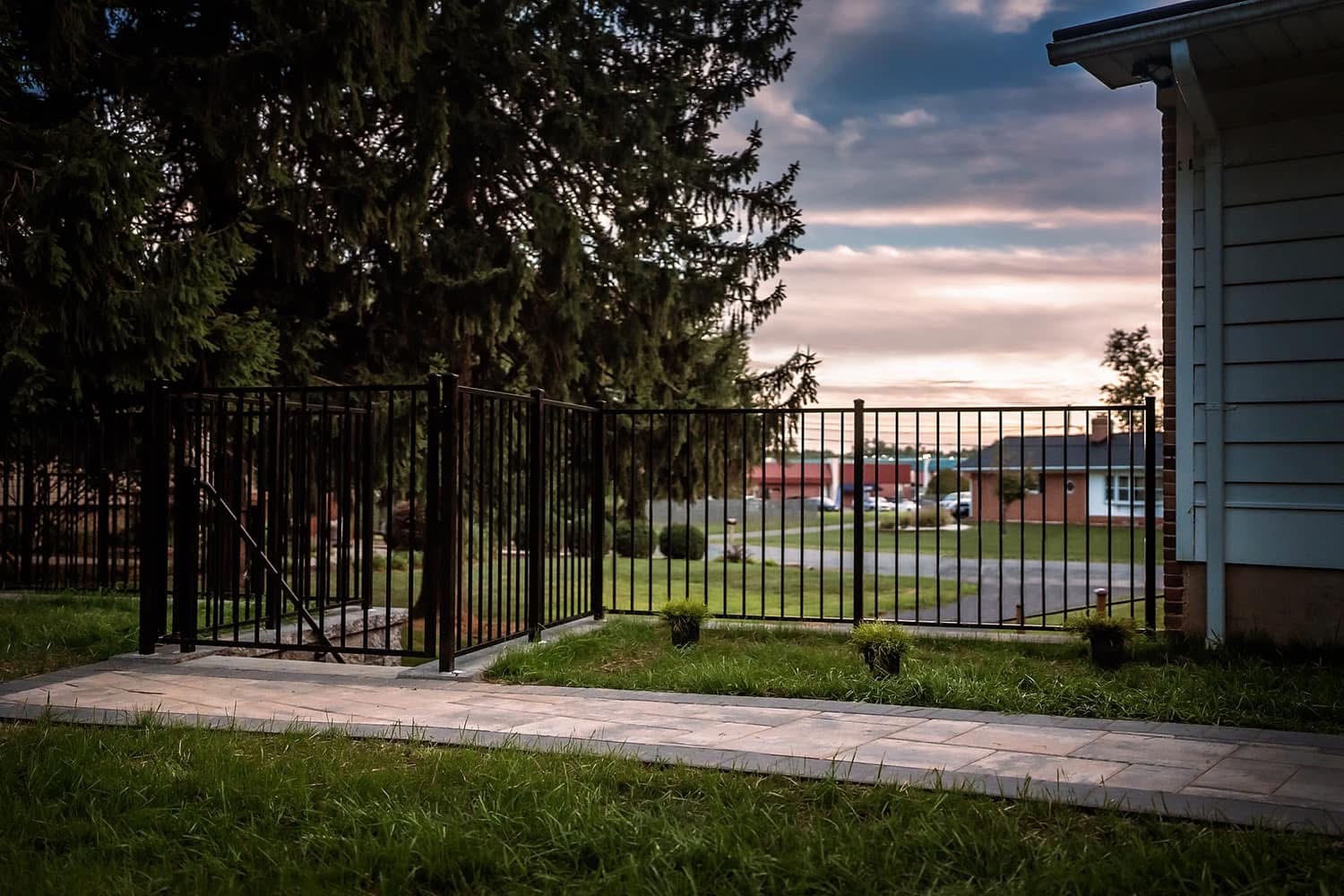 Black aluminum fence with gate at sunset